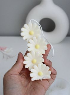 a hand holding some white flowers in front of a vase and toilet paper roll holder