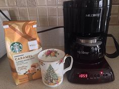 there is a coffee maker and cup on the counter next to some coffee bags, which are also being used as an alarm clock