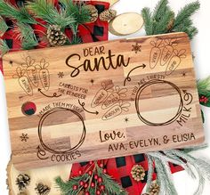 personalized wooden cutting board with christmas decorations and pine cones on it, surrounded by evergreen branches