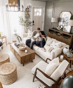 two people sitting on a couch in a living room with white furniture and rugs