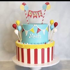 a circus themed birthday cake with balloons and streamers on the top is blue, red, yellow and white