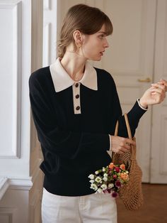 a woman holding a basket with flowers in it and wearing a black sweater over white pants