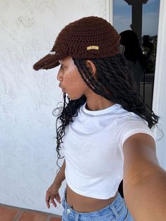 a woman with dreadlocks wearing a brown hat and white t - shirt standing in front of a door