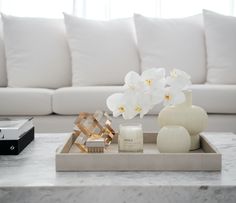 a living room with white furniture and flowers on the coffee table in front of it