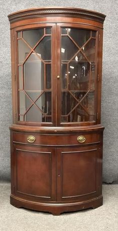 a wooden china cabinet with glass doors on the top and bottom, sitting against a wall