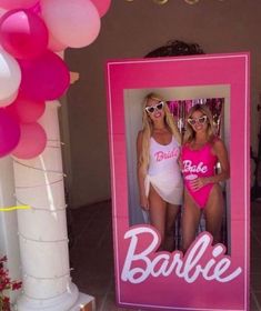 two women in swimsuits standing behind a barbie photo frame with balloons and streamers