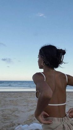 a woman sitting on top of a sandy beach next to the ocean