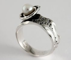 "Here is the ring \"Flower of sea\" in sterling silver and white freshwater pearl. Each ring is unique, the lace around the dome that hosts the pearl is unique each time and may be different from the photo. Size: 7 mm width (9/32 in) Material: Sterling silver and white freshwater pearl The unique texture of the ring is made from a molding of a sea urchin shell symbolizing a footprint of good times. This organic texture was handcrafted by the jeweler Marie-Eve Bordeleau of Trois-Rivières, Quebec, Canada. Included: -A polishing cloth -A bookmark about the collection -A rigid box ** Shipping fees are free in Canada and the United States Inspiration: The shell of the sea urchin inspires emotions, feelings and memories. The unique impressions left by the shells symbolize a true story, a trip or Sterling Silver Open Pearl Ring, Sterling Silver Open Pearl Ring Fine Jewelry, Elegant White Gold Pearl Ring Stamped 925, Sterling Silver White Gold Pearl Ring With Pearl Drop, White Gold Sterling Silver Rings With Pearl Drop, White Gold Pearl Drop Ring In Sterling Silver, Sterling Silver Pearl Drop Ring In White Gold, Handmade White Gold Pearl Ring For Formal Occasions, Elegant Silver Pearl Ring Stamped 925