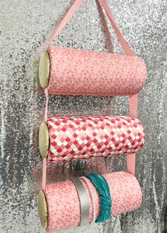 three rolls of fabric are hanging on a pink rack with two green and white ribbons