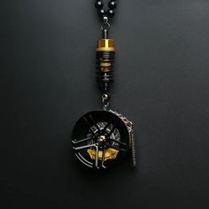 a black and gold necklace with a clock on it's back end, hanging from a chain