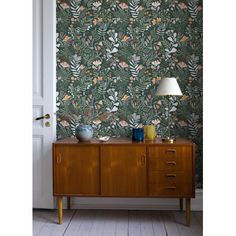 a sideboard with a lamp on it in front of a wallpapered room