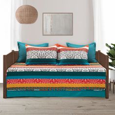 a bed with colorful sheets and pillows in a room next to a potted plant