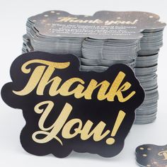 a pile of black and gold thank you cards next to stacks of silver and gold coasters