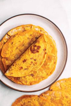 three tortillas on a white plate next to two slices of bread in the background