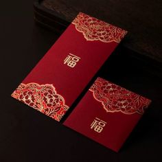 two red cards with gold designs on them sitting next to a wooden box and black background