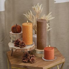 three candles sitting on top of a wooden table next to pine cones and pumpkins