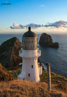 a white lighthouse sitting on top of a grass covered hill next to the ocean and cliffs