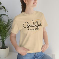 Celebrate the power of gratitude with our 'A Grateful Heart' T-Shirt. Made from high-quality cotton materials, this graphic tee is soft, comfortable, and perfect for everyday wear. Show the world that a grateful heart is a happy heart with this stylish and meaningful tee. Whether you're layering or wearing it on its own, this shirt is a great way to spread positivity and spread the message of thankfulness. Custom made 100% cotton Light fabric Retail fit Tear away label Runs true to size Cotton T-shirt With Heart Graphic For Fall, Cotton Heart Graphic T-shirt For Fall, Inspirational Crew Neck T-shirt For Fall, Fall Cotton T-shirt With Heart Graphic, Casual T-shirt With Heart Graphic For Gift, Casual Relaxed Fit Tops As A Gift, Casual Relaxed Fit Tops For Gifts, Inspirational Cotton T-shirt For Fall, Casual Soft-washed T-shirt Gift