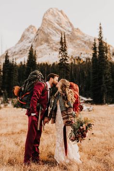 a bride and groom kissing in front of a mountain with their backpacks on his back