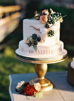 a white wedding cake with flowers on the top is sitting on a gold stand outside