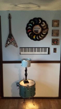 a drum sits on the floor in front of a wall with musical instruments hanging above it