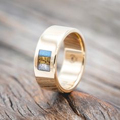 a gold ring with a blue and yellow stone in the center on a wooden surface