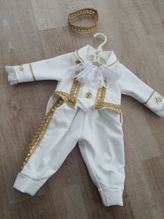 a baby's white and gold outfit is laying on the floor