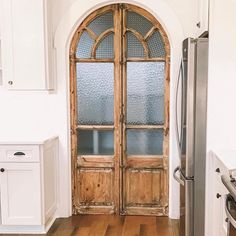 an open door leading into a kitchen with wood floors and white walls, in front of a stainless steel refrigerator