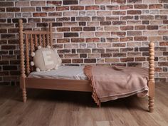 a wooden bed with a blanket on it in front of a brick wall and hardwood floor