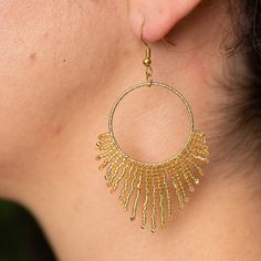 Illuminate your ensemble with the Golden Sun Earrings, a dazzling expression of craftsmanship and elegance. Each earring features a radiant gold circle, exquisitely framed by a shimmering gold fringe of miyuki glass beads, all intricately handwoven to perfection. Pair them with your favorite attire to create a look that shines from day to night. While these earrings stand beautifully on their own, they can be complemented by the Golden Sun Necklace, sold separately, to complete the resplendent s Gold Fringe Metal Chandelier Earrings, Gold Fringe Chandelier Earrings, Gold Earrings With Beads For Celebration, Gold Round Earrings With Gold Beads, Gold Fringe Earrings In Brass, Gold Beaded Earrings With Ear Wire For Party, Gold Beaded Hoop Earrings For Party, Gold Hoop Earrings With Beads For Party, Gold Bohemian Tassel Earrings For Festive Occasions