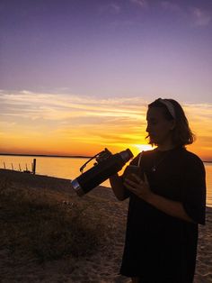 a woman standing on top of a beach next to the ocean holding a water bottle