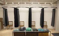 two tables with clothes on them in front of black curtains and white tiled walls behind them