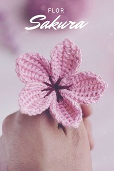 a pink crocheted flower sitting on top of someone's hand with the words, flor sakiura written above it