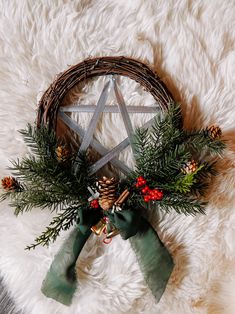 a wicker wreath with evergreen, pine cones and berries on it sits in front of a white rug