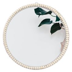 a round mirror with white beaded trim around it and a green plant in the middle