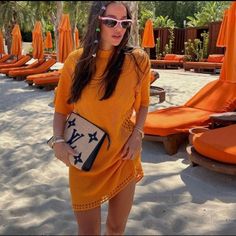 a woman in an orange dress is standing on the beach with sun umbrellas behind her