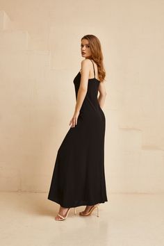 a woman in a long black dress is standing against a wall and looking off to the side