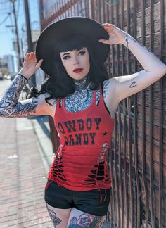 Sexy cowgirl wearing a red slashed and braided tank top that says cowboy candy in black western print with ribcage sleeve cutouts and braiding for a sexy country festival wardrobe look! Cowboy Pinup, Stagecoach Outfit, Cowboy Candy, Hourglass Waist, Country Festival, Biker Outfit, Pin Up Outfits, Festival T Shirts, Goth Women