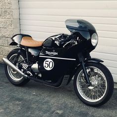 a black triumph motorcycle parked in front of a garage door with the number 50 on it