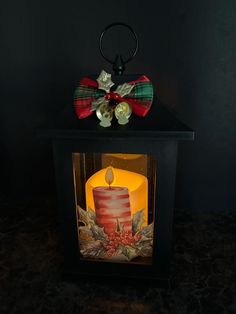 a lit candle with a bow on it sitting in front of a black box that is decorated with holly and berries