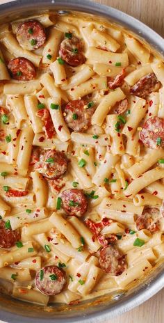 a pan filled with pasta and sausages on top of a wooden table next to utensils