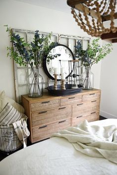 a bedroom with a bed, dresser and clock on it's side wall next to a chandelier