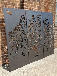 three metal panels with designs on them sitting in front of a brick wall and sidewalk