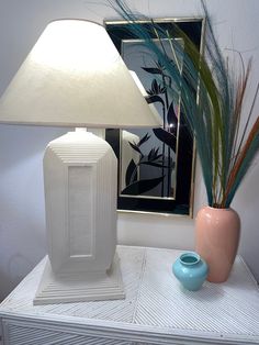 a table with a lamp and vase on it, next to a framed art piece