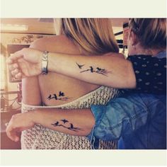 two women with matching tattoos on their arms, one is holding the other's arm