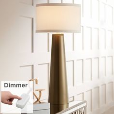 a lamp that is sitting on top of a table next to a hand holding a remote control