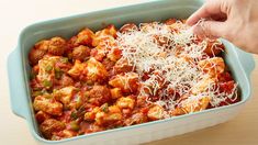 someone is sprinkling parmesan cheese on top of some food in a casserole dish