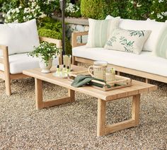 a wooden table sitting on top of a gravel covered ground next to two white couches