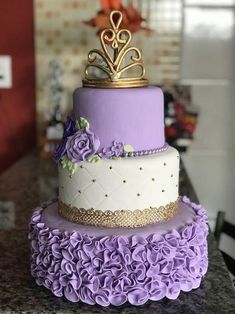 a three tiered cake with purple flowers and a gold crown on top is sitting on a counter