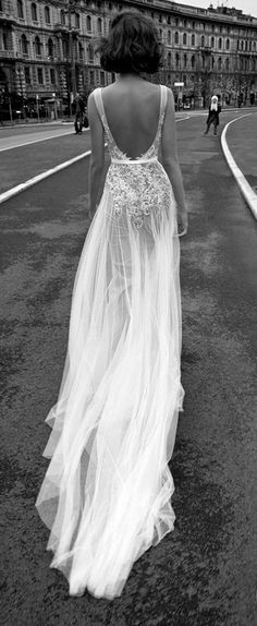 a woman is walking down the street in a long white dress with an open back